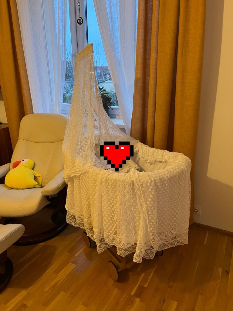 Das Bild zeigt einen Stubenwagen mit weißem Spitzenstoff und einem verpixelten Herz in der Mitte.